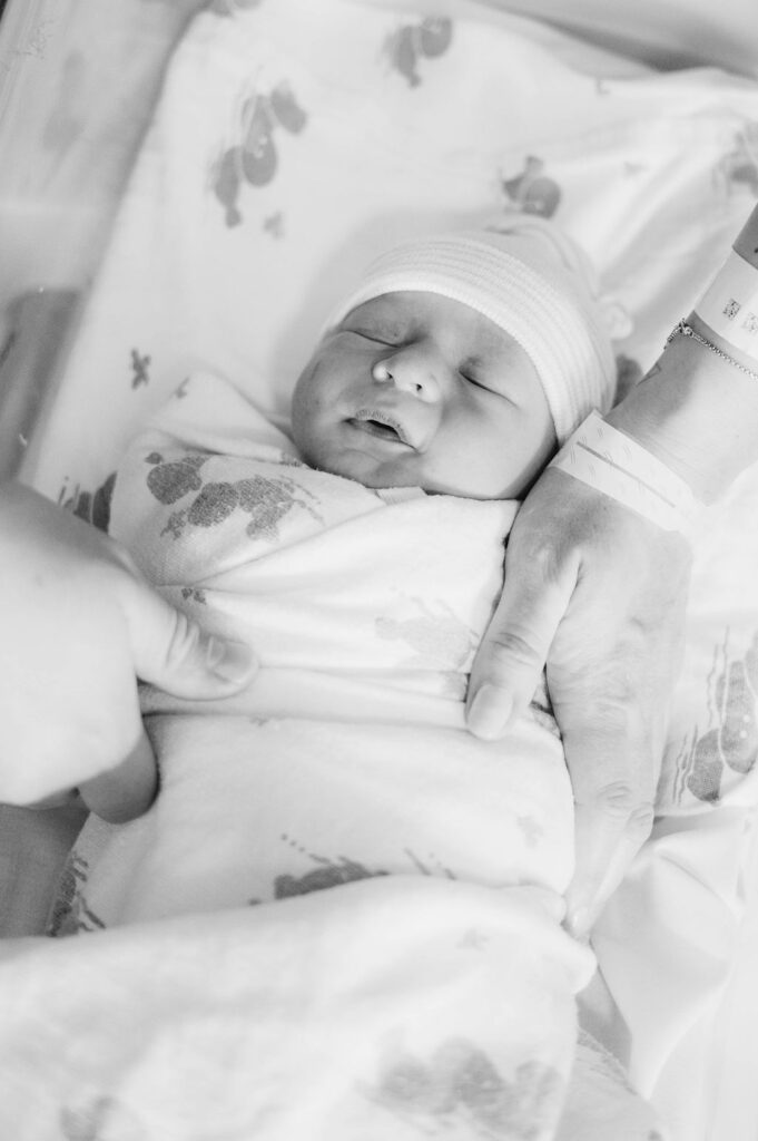 Black and white image of newborn son with mom and dad's hands