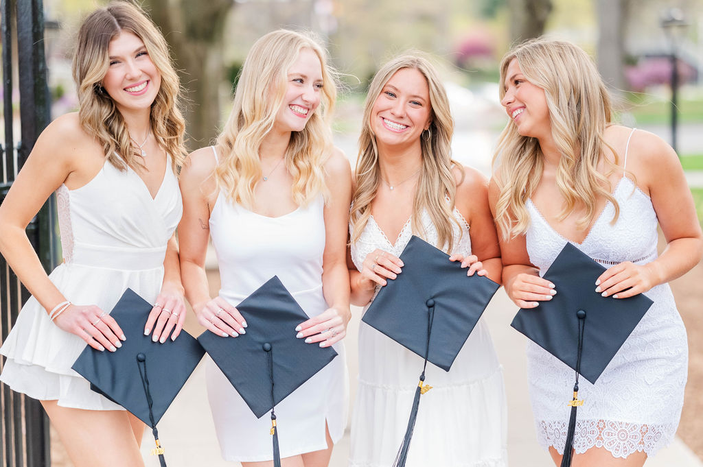 Four grads holding caps and laughing with each other