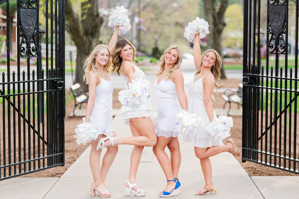 Four college grads posing with their dance team pom poms