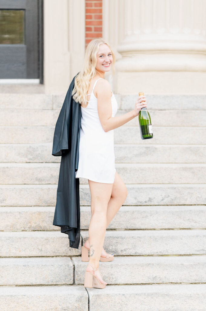 College grad holding gown and champagne on stairs at Worcester State University