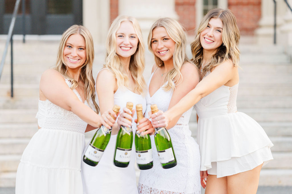 Four college grads saying cheers with their champagne bottles