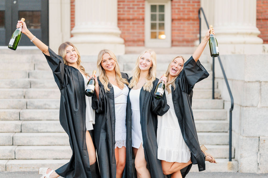 Four girls dressed in their cap and gown celebrating with champagne