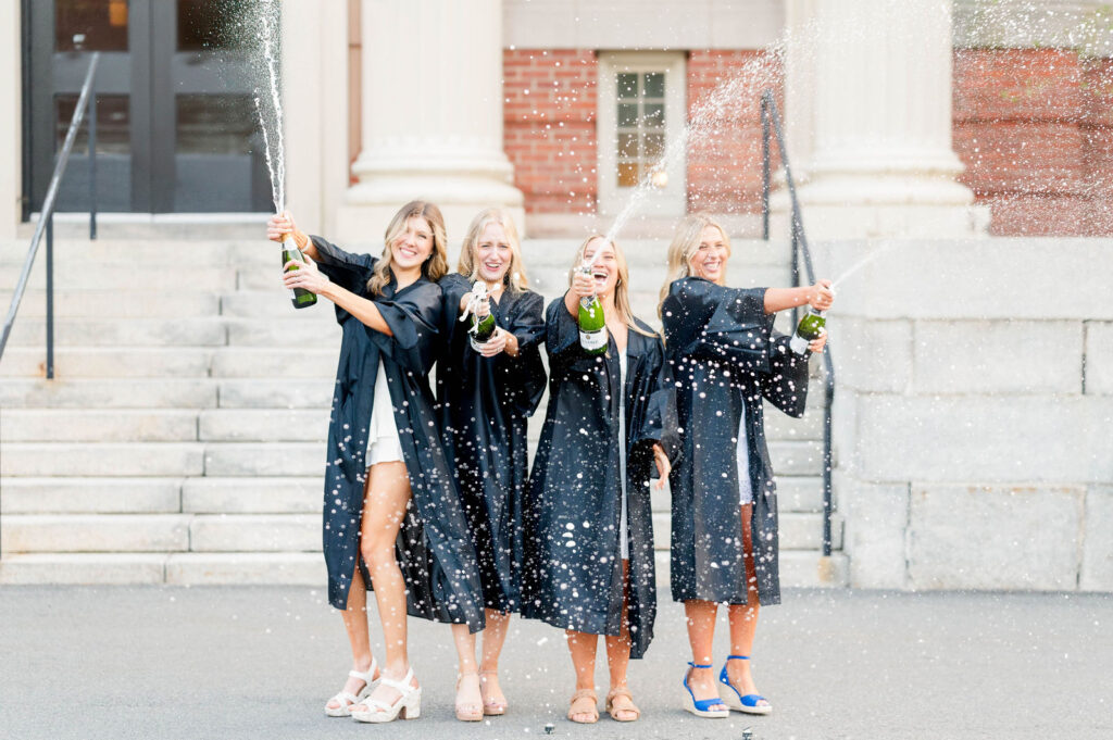 Four girls in cap and gown at Worcester State University doing a champagne spray 