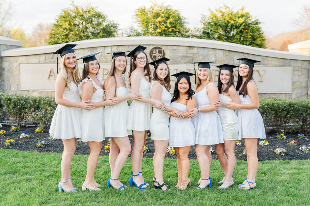Group of college girls wearing cap posing in front of the Assumption University sign