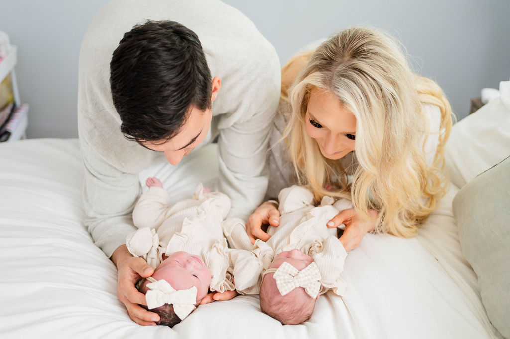 mom and dad looking at twin newborns on bed