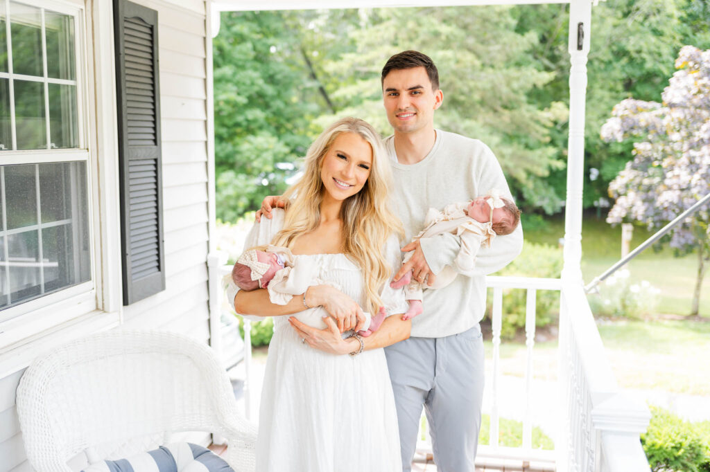 man and woman holding newborn baby girls on porch in their rhode island home