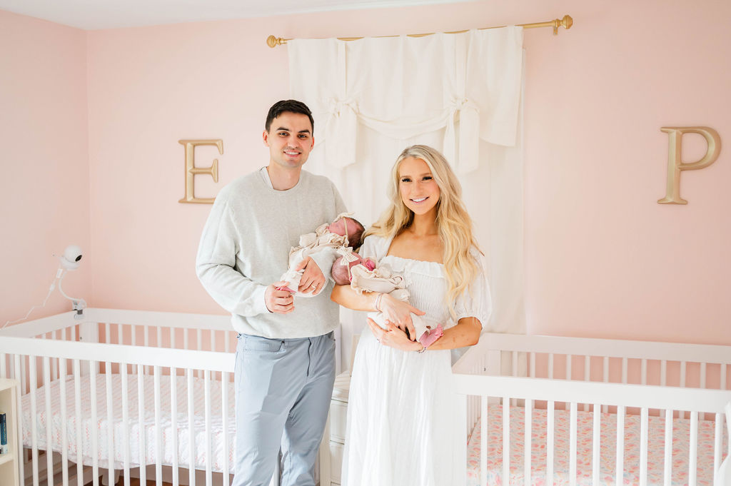 Rhode Island newborn photographer's image of a mom and dad in pink nursery holding twin girls