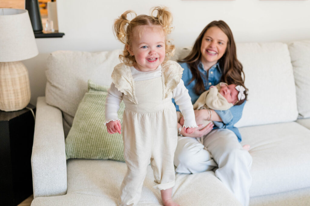 Little toddler girl smiling with mom and newborn in the background
