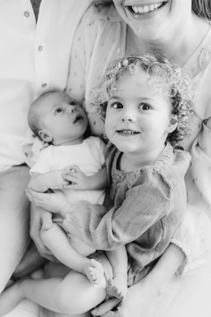 big sister smiles while holding baby brother