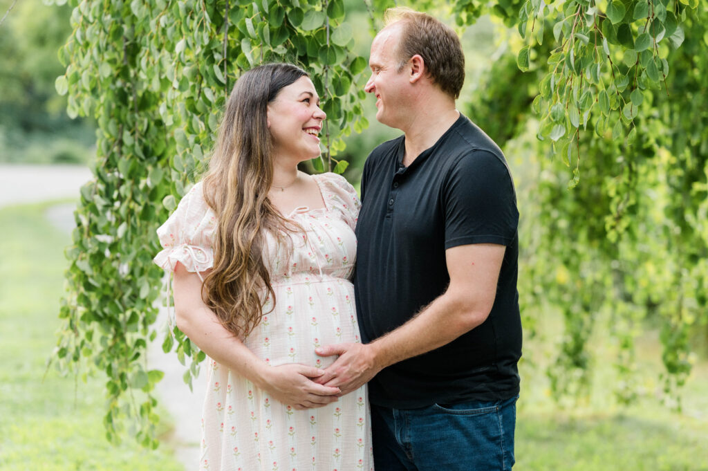 Close up shot by the willow tree at the arnold arboretum of husband and wife smiling at each other