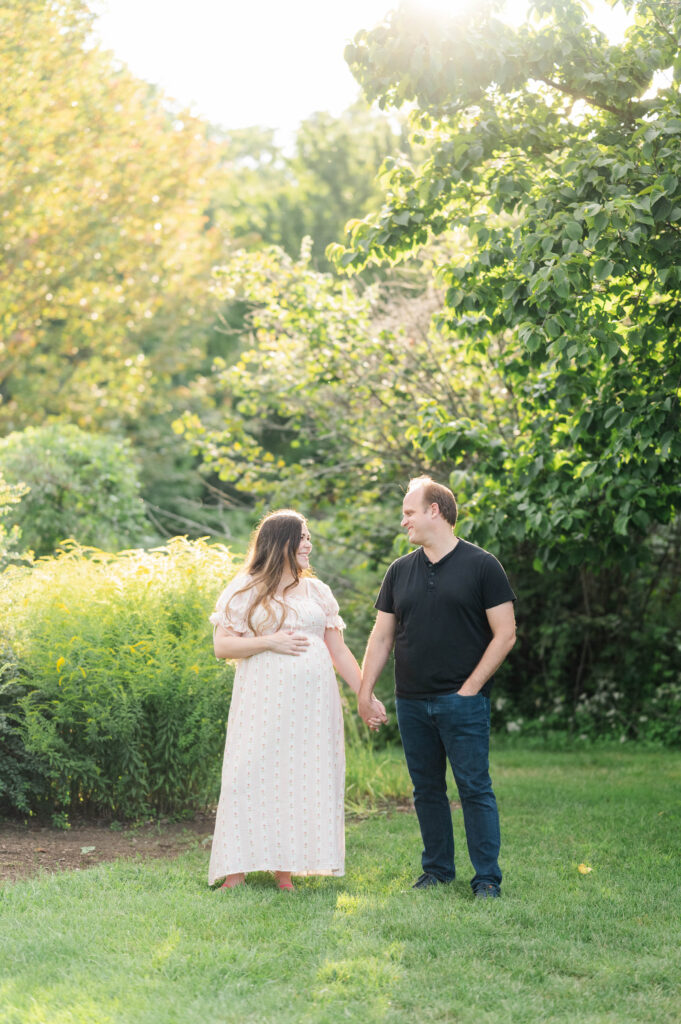 Husband and wife holding hands smiling at each other during maternity shoot at arnold arboretum