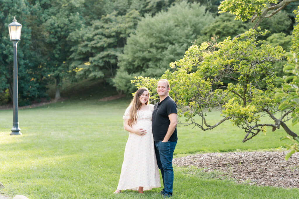 Expectant mom and husband smiling at the camera at the Arnold Arboretum for a maternity shoot in Boston